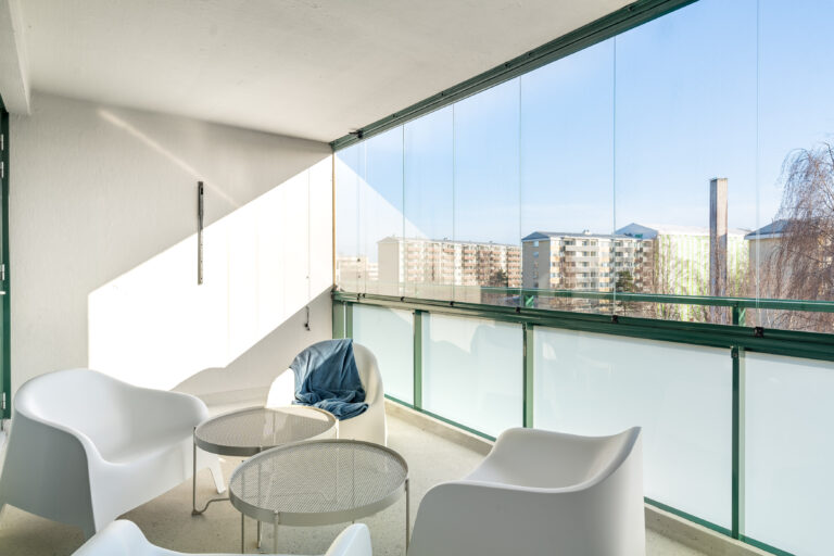 Large glazed balcony with outdoor furniture and views of greenery, offering a peaceful private space for students in modern student housing